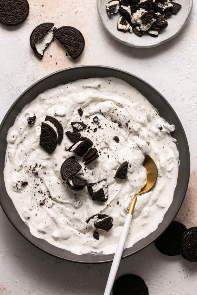 Oreos being mixed into the Oreo cream fluff mixture in a bowl with a spoon.