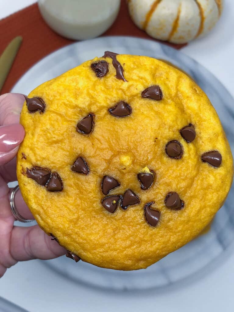 A hand holding a pumpkin chocolate chip cookie.