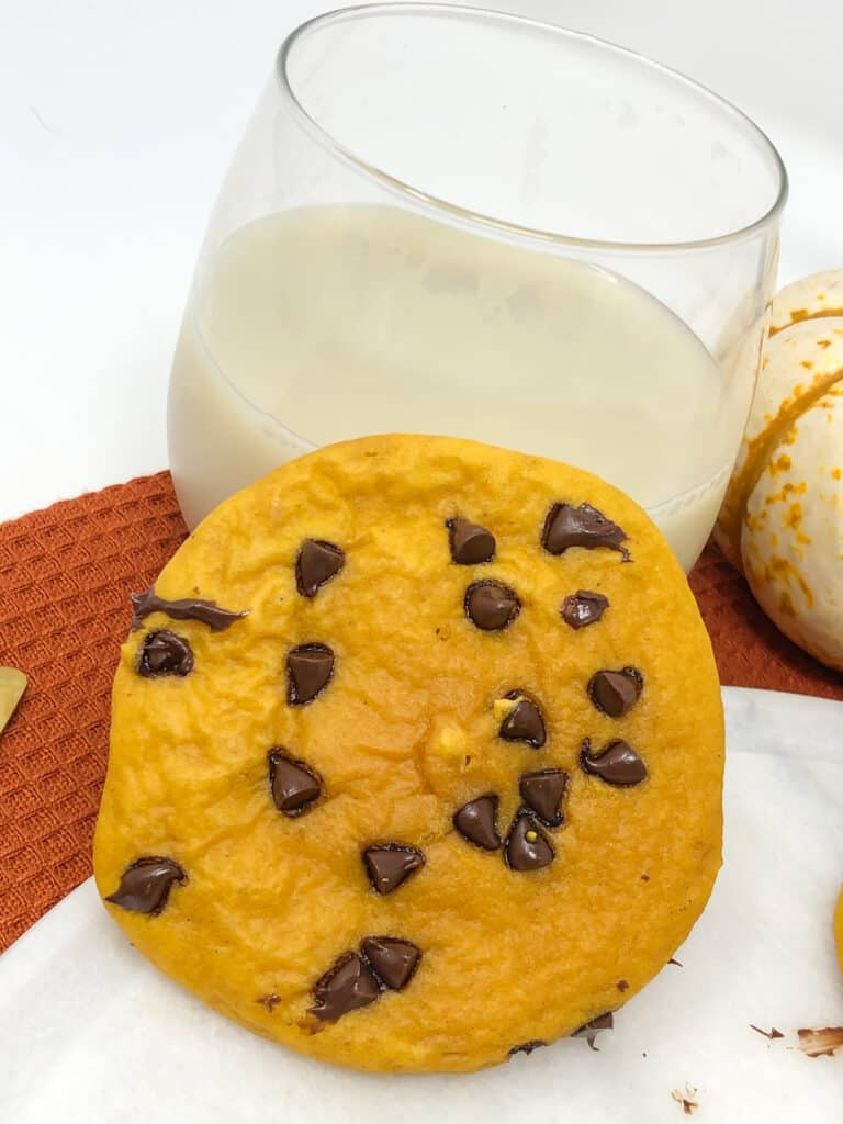 A pumpkin chocolate chip cookie with  a glass of milk.