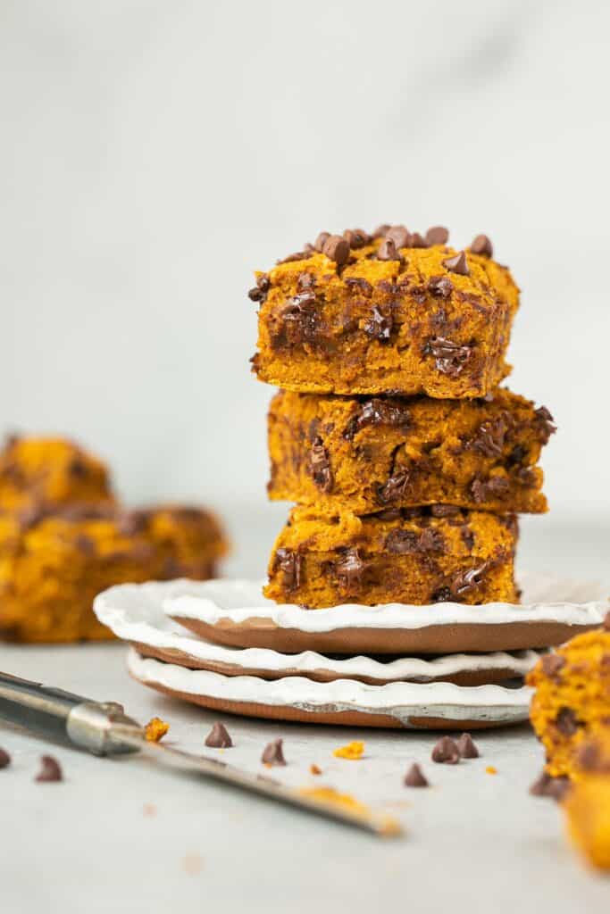 Healthy pumpkin chocolate chip blondies stacked on top of each other on a small plate.