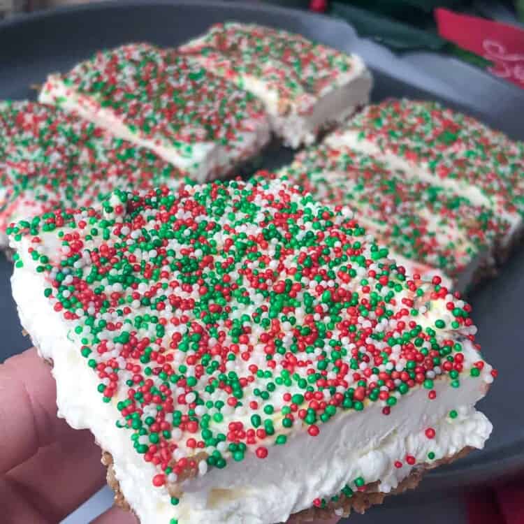 A hand holding a Christmas cheesecake crunch bar topped with red and green sprinkles.
