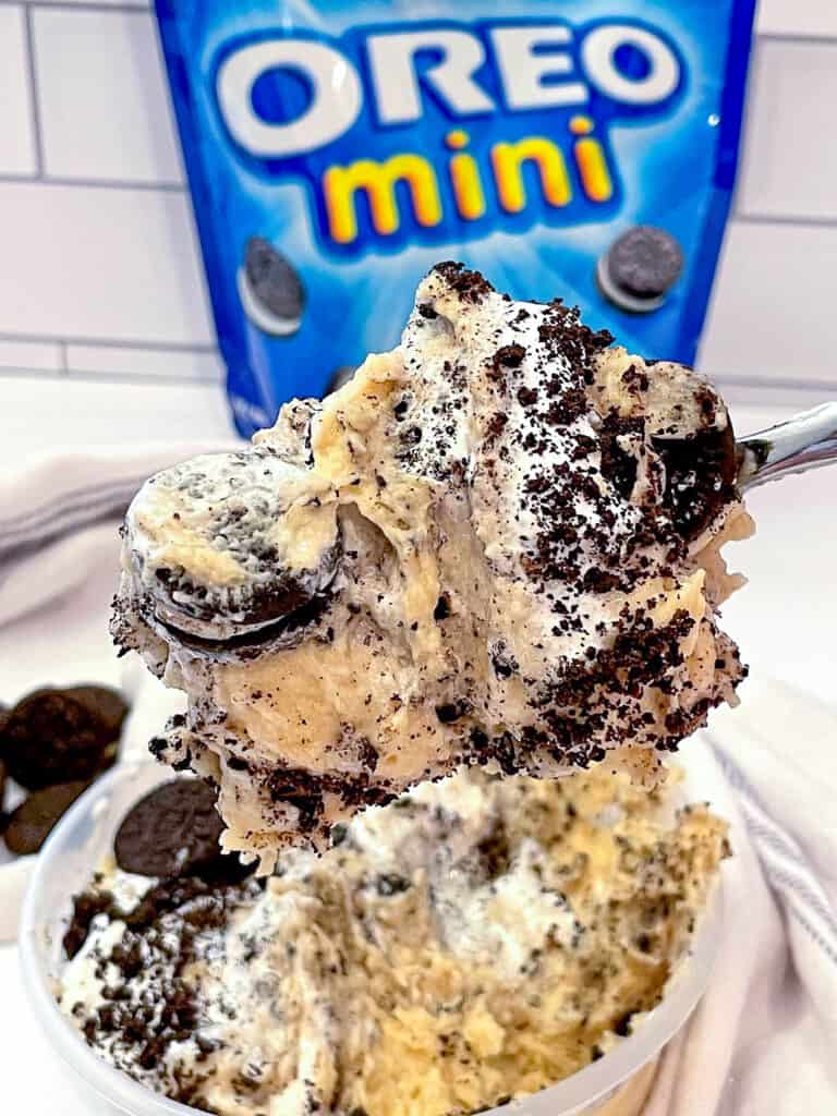 Protein cookie dough topped with addtional oreo cookie pieces in a bowl being served with a spoon.