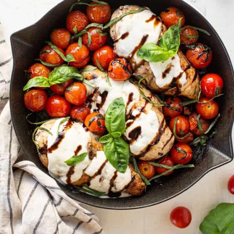 Chicken Caprese in a skillet surrounded by charred tomatoes and topped with balsamic