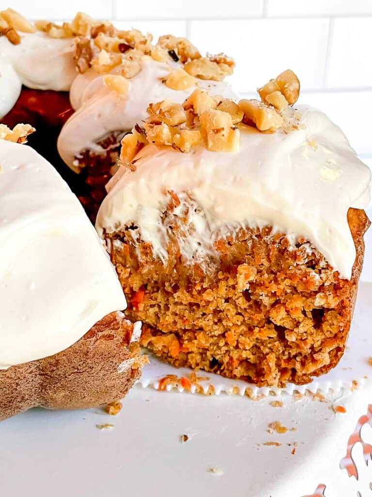 Healthy carrot cake topped with cream cheese frosting and chopped nuts on a plate.