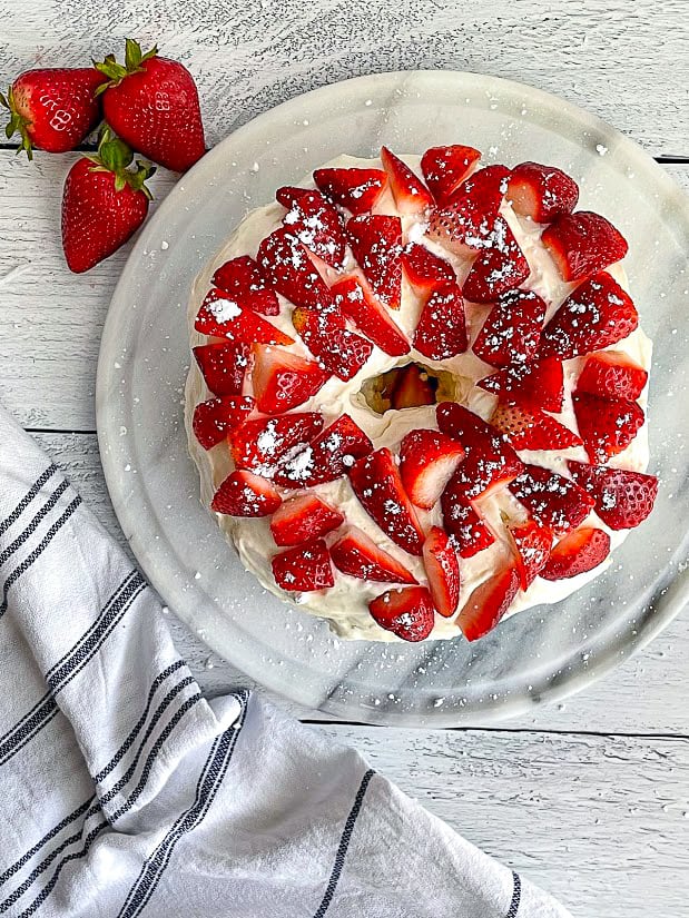 Healthy protein angel food cake topped with frosting and strawberries on a plate.