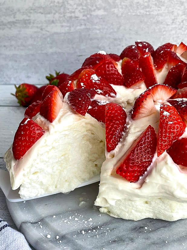 Zoomed in view of healthy protein angel food cake topped with strawberries on a cooling rack.