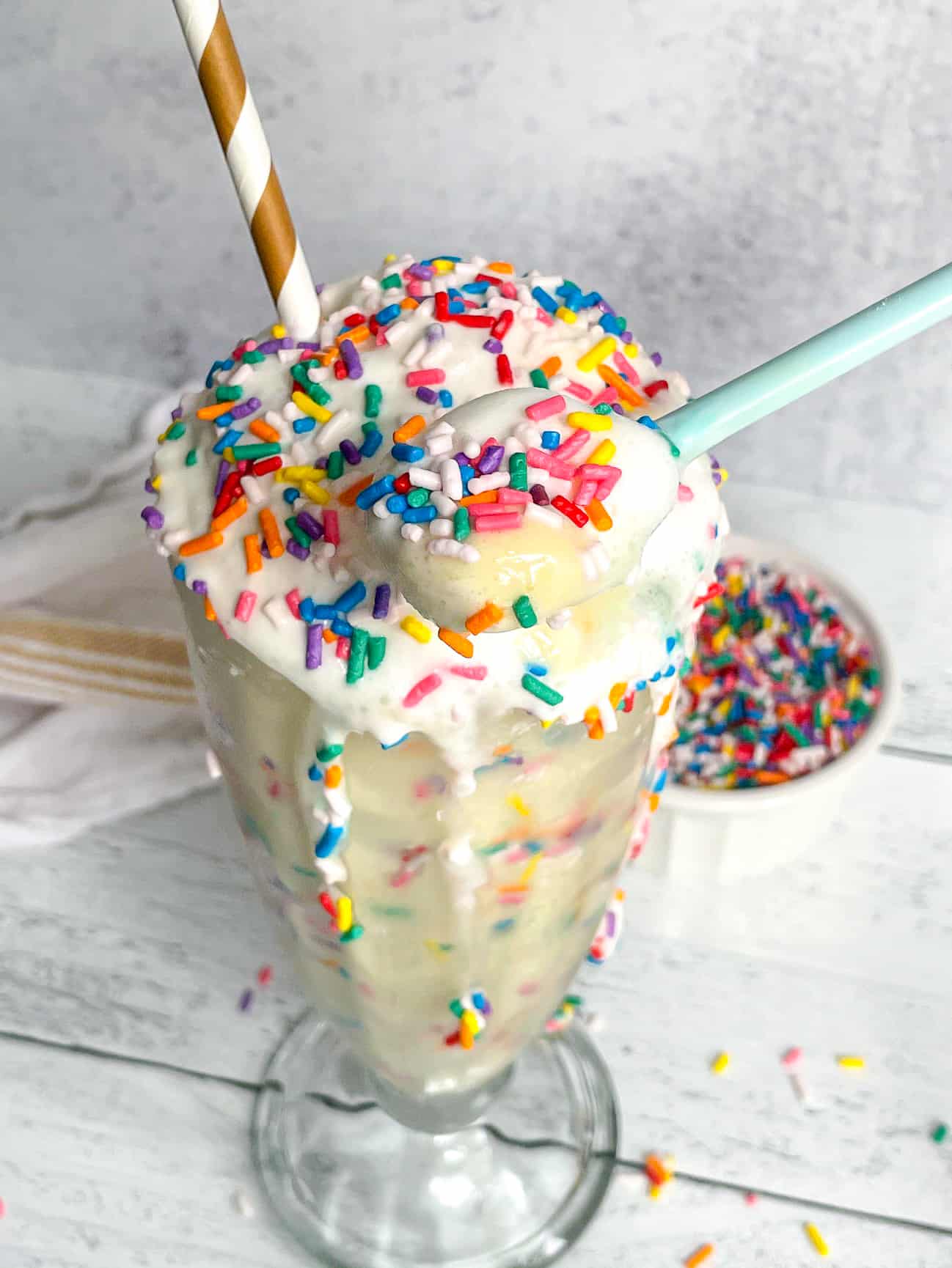 Birthday Cake Protein Milkshake with rainbow sprinkles and a paper straw