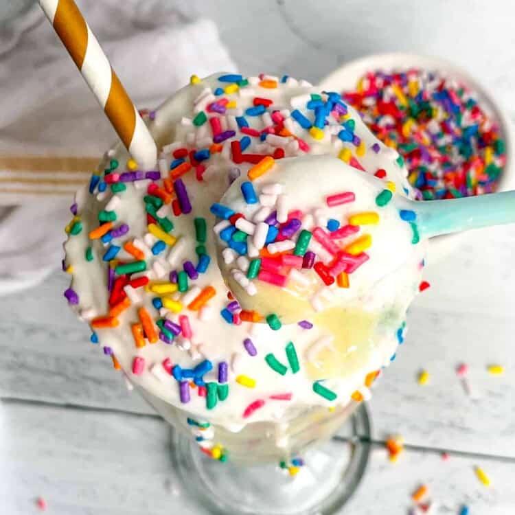 Birthday Cake Protein Milkshake with rainbow sprinkles and a paper straw