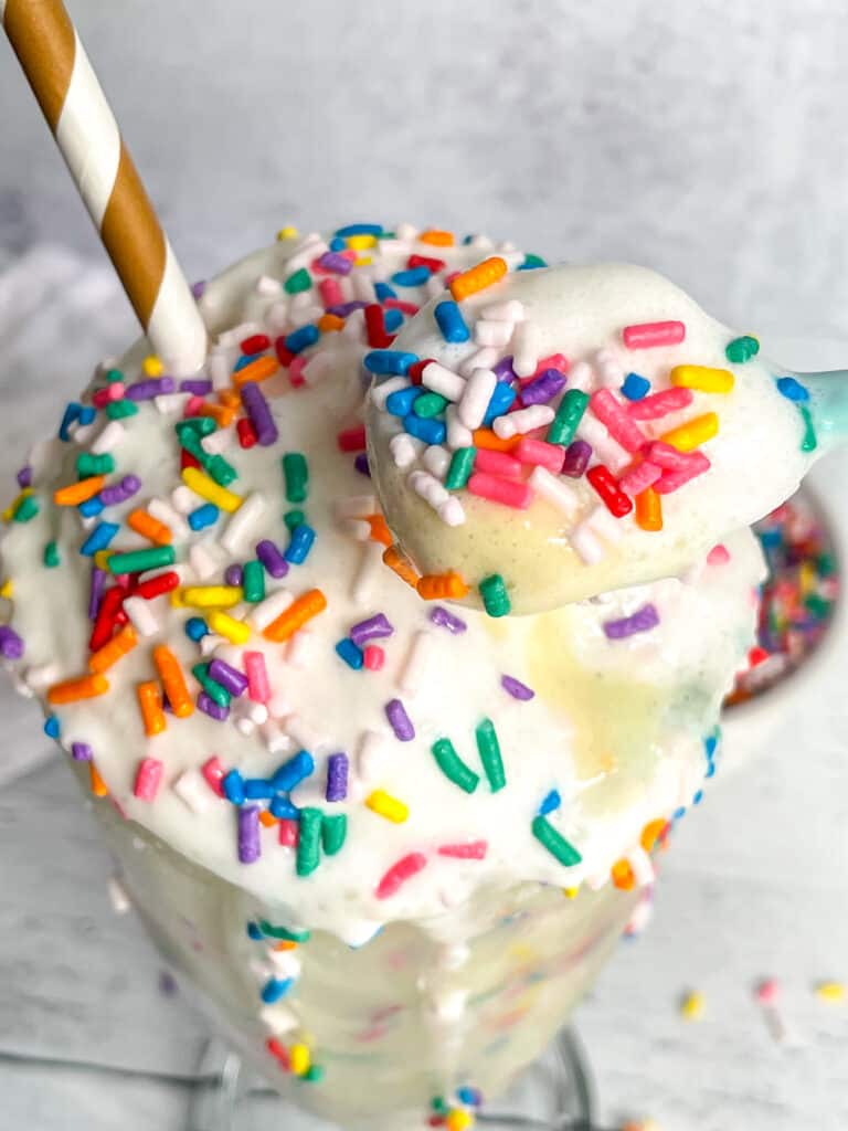 Birthday Cake Protein Milkshake with rainbow sprinkles and a paper straw.