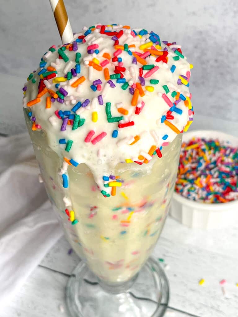Birthday Cake Protein Milkshake with rainbow sprinkles and a paper straw.