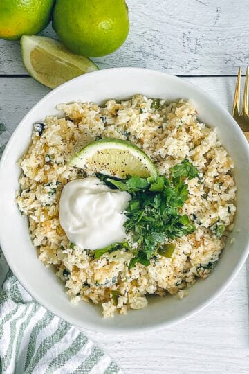 bowl of cilantro lime cauliflower rice in a bowl topped with a lime wedge and cilantro for garnish