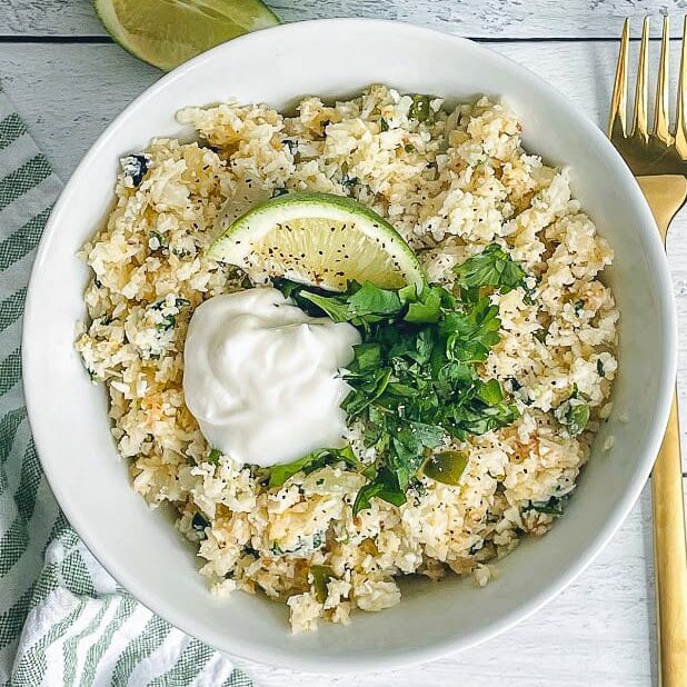 bowl of cilantro lime cauliflower rice in a bowl topped with a lime wedge and cilantro for garnish