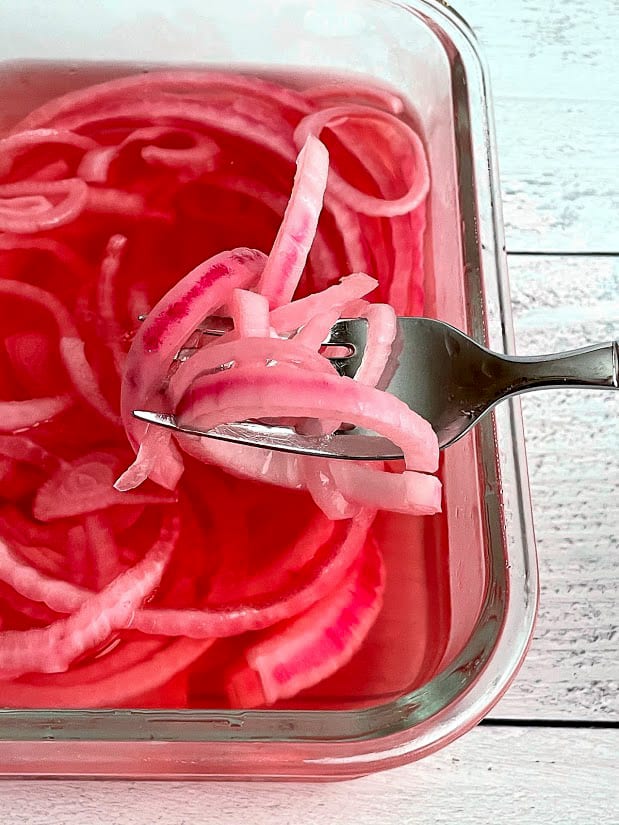 Forkful of cold pickled red onions in a tupperware container