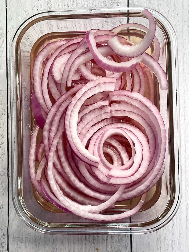 sliced red onions in a tupperware filled with vinegar