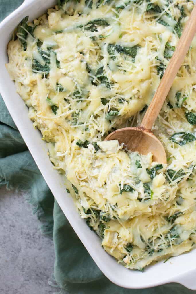 Spinach and artichoke spaghetti squash bake in a baking dish with a wooden spoon.