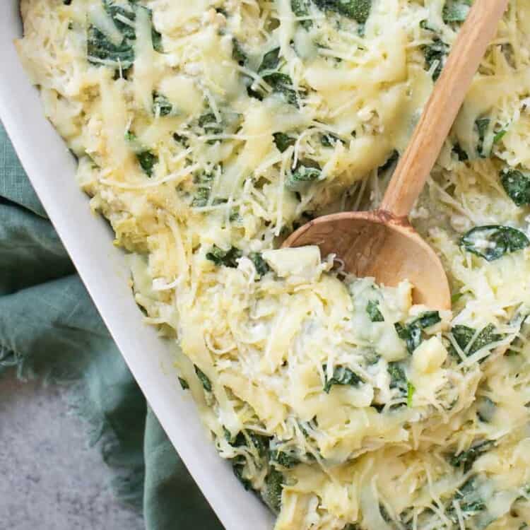 Spinach and artichoke spaghetti squash bake in a baking dish with a wooden spoon.