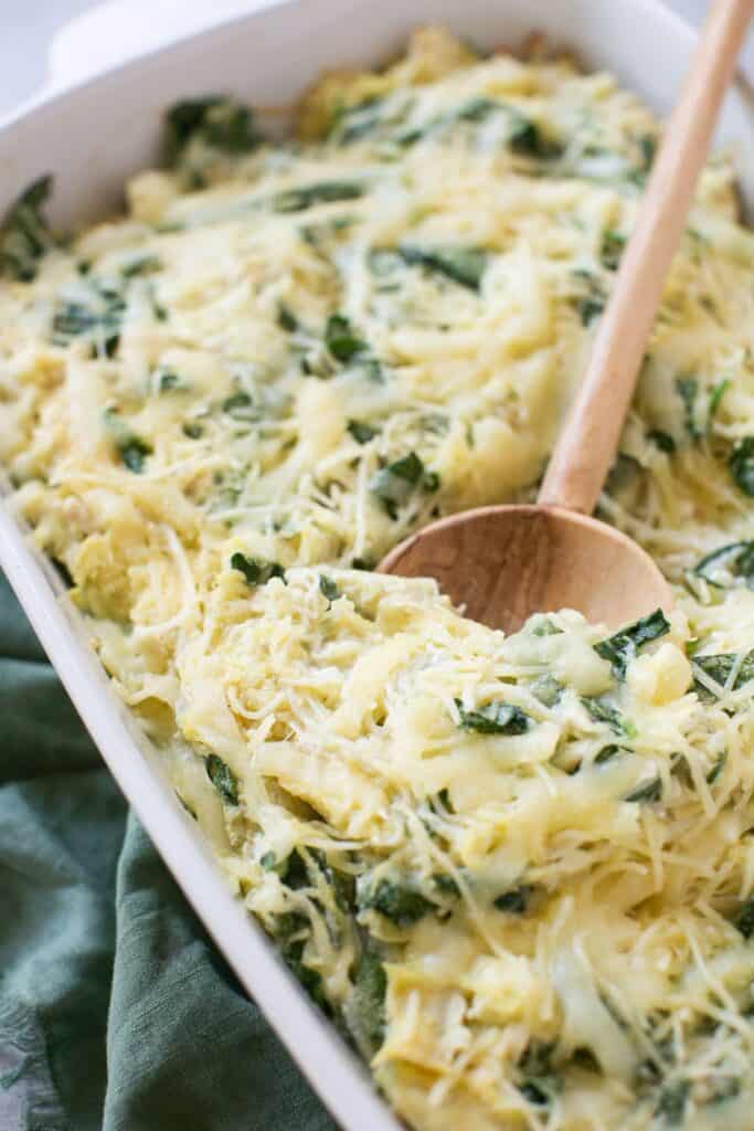 Zoomed in view of spinach and artichoke spaghetti squash bake in a baking dish with a wooden spoon.