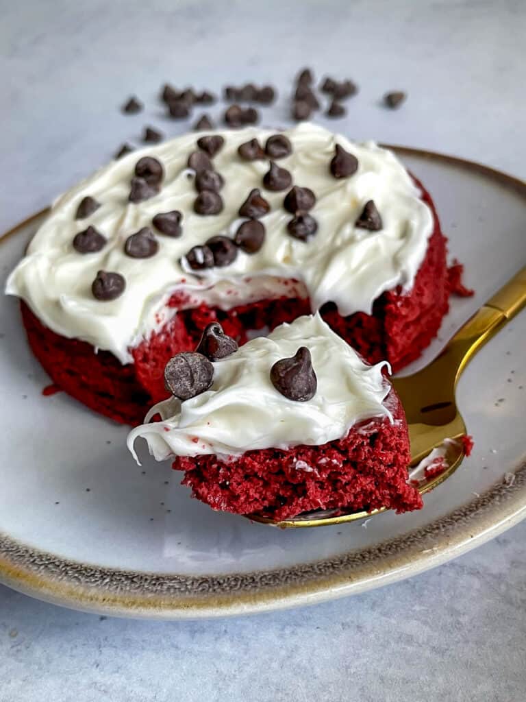 Red velvet mug cake topped with frosting and chocolate chips on a plate with a fork.