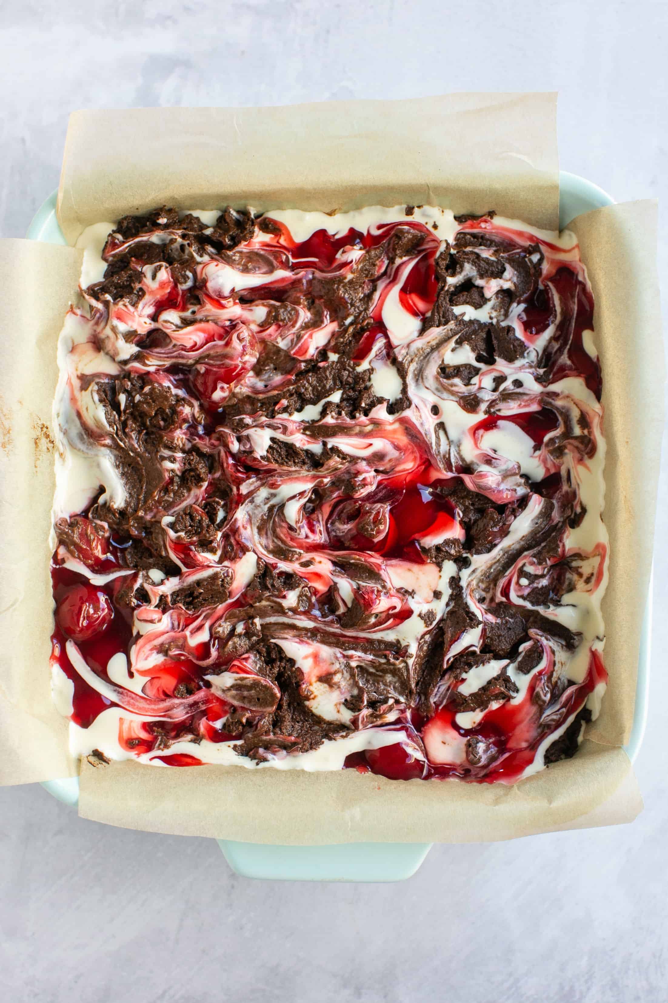 Cherry cheesecake brownie batter in a square baking dish after being swirled together.