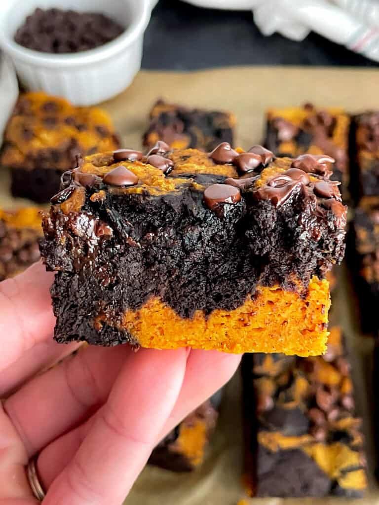 A hand holding a fudgy pumpkin swirl brownie with additional brownies in the background.