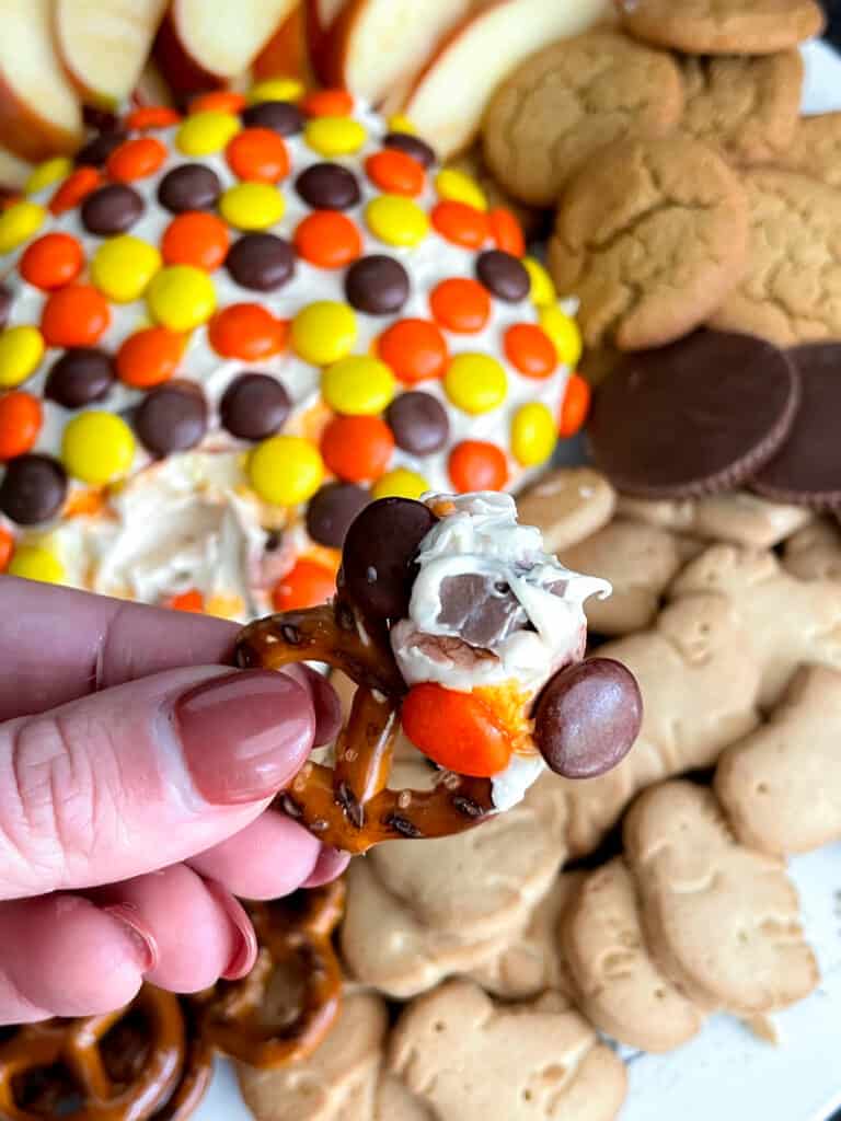 A hand holding a pretzel topped with peanut butter cheese ball.