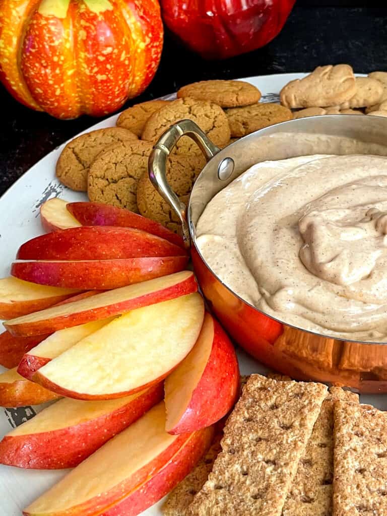 Zoomed in view of skinny pumpkin dip on a tray with apple slices, graham crackers, pretzels, animal crackers, and cookies.