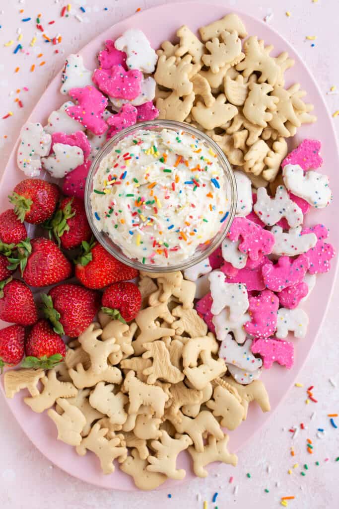 Dunkaroo dip in a bowl topped with sprinkles served with animal crackers, animal cookies, and strawberries