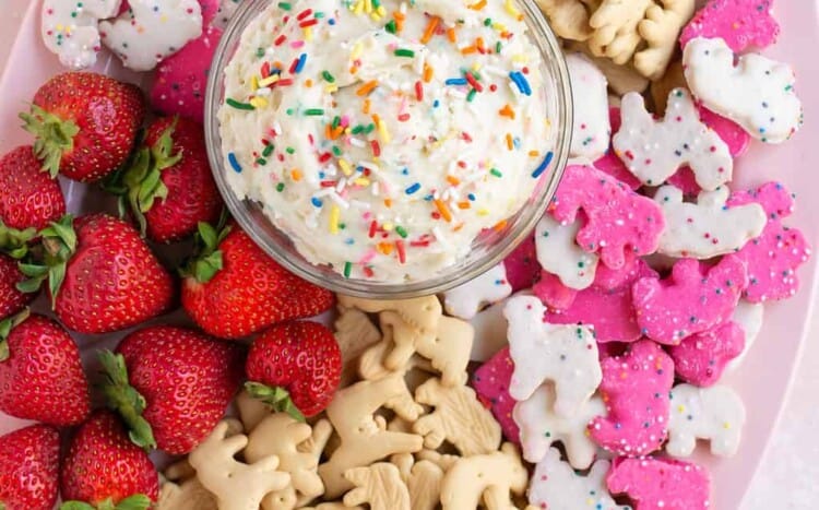 Dunkaroo dip topped with sprinkles in a small bowl with strawberries and animal cracker on the side.