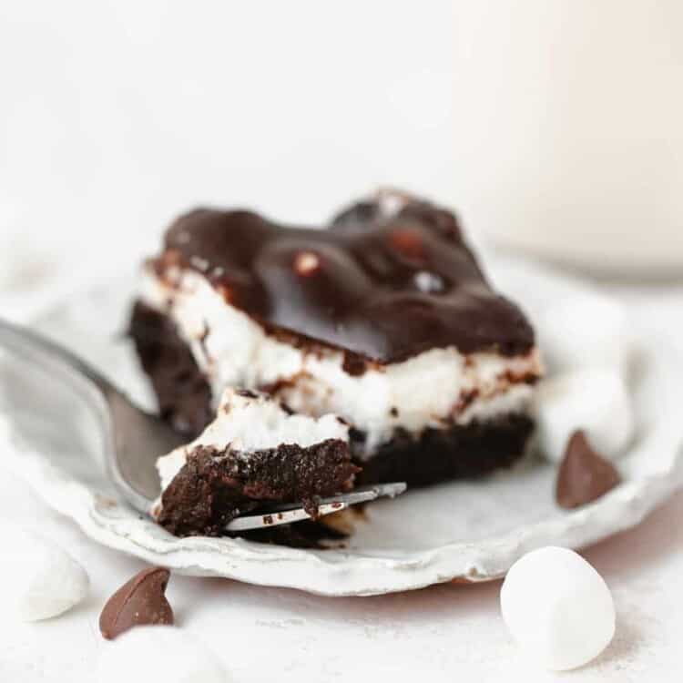 One Mississippi Mud Brownie on a white plate with a fork surrounded by marshmallows and chocolate chips.