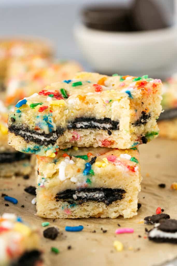 Two Cake Batter Oreo Blondies stacked on top of each other with a bite taken out of the top one.