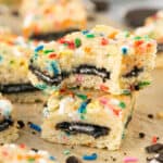 Two Cake Batter Oreo Blondies stacked on top of each other with a bite taken out of the top one.