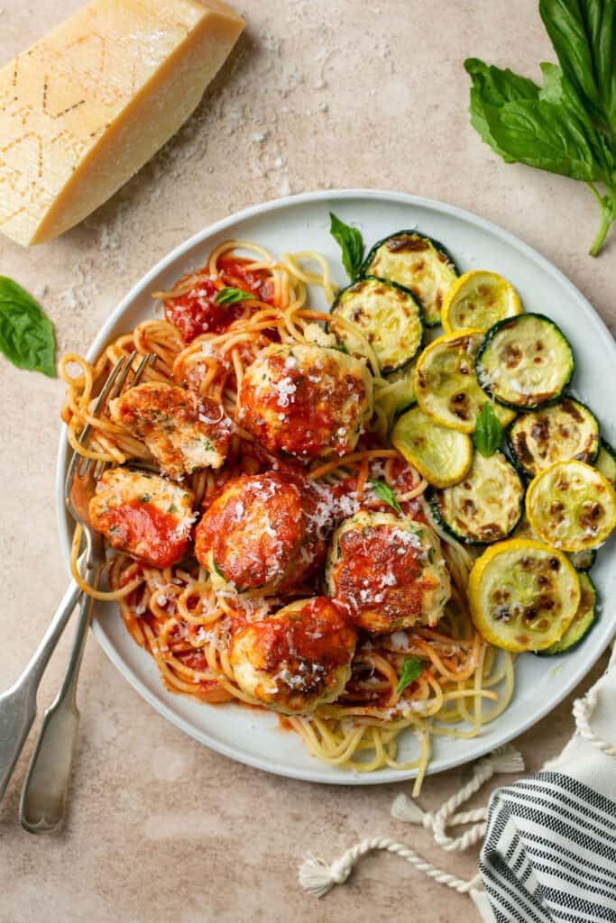Turkey ricotta meatballs served over spaghetti with a side of roasted zucchini on a plate.
