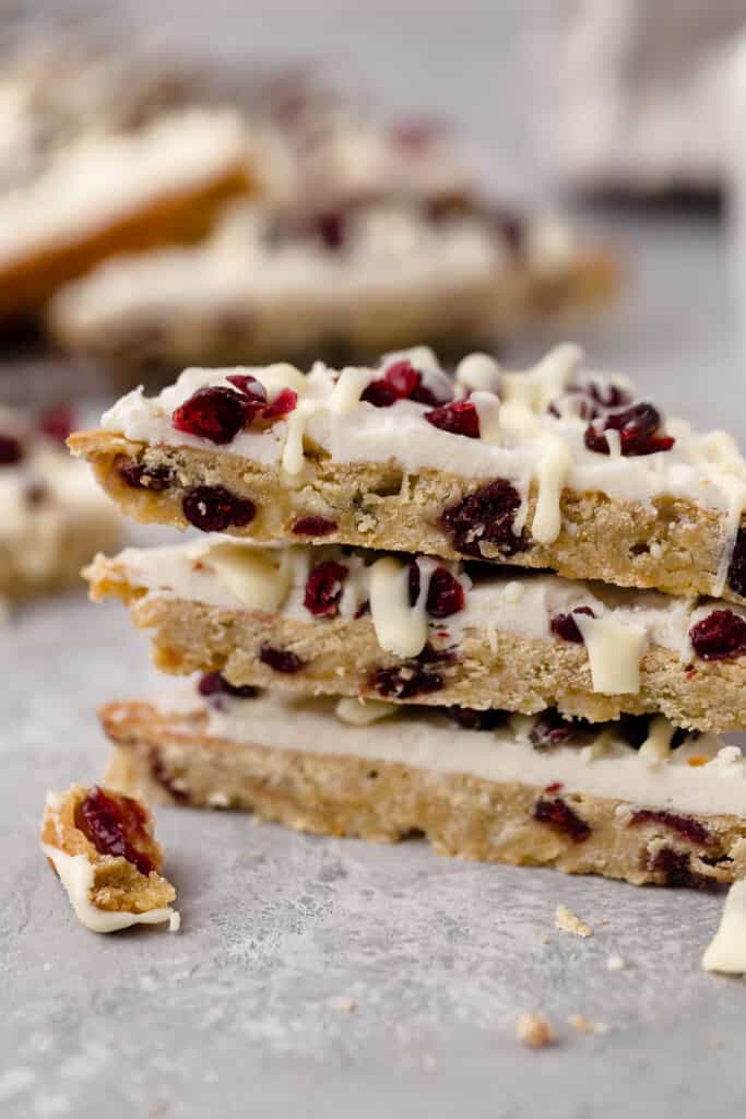 Cranberry bliss bars stacked vertically on parchment paper.