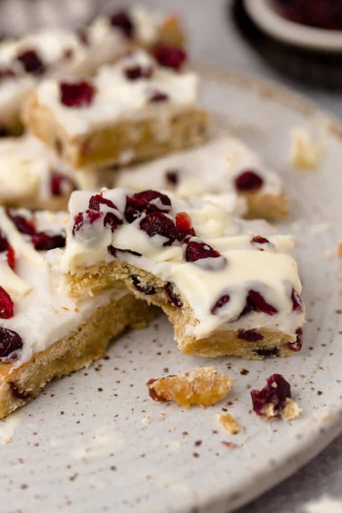 Zoomed in view of cranberry bliss bars on parchment paper, one with a bite taken out of it.