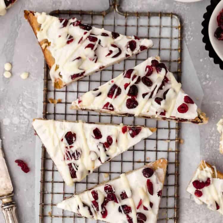 Cranberry bliss bars cut into triangles on a cooling rack.