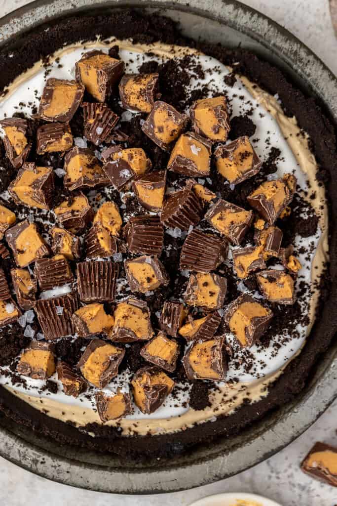 No bake oreo peanut butter pie topped with chopped Reese's with one in a pie dish.