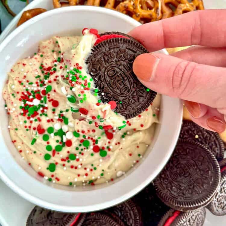 A hand dipping an oreo in sugar cookie dip in a small bowl.