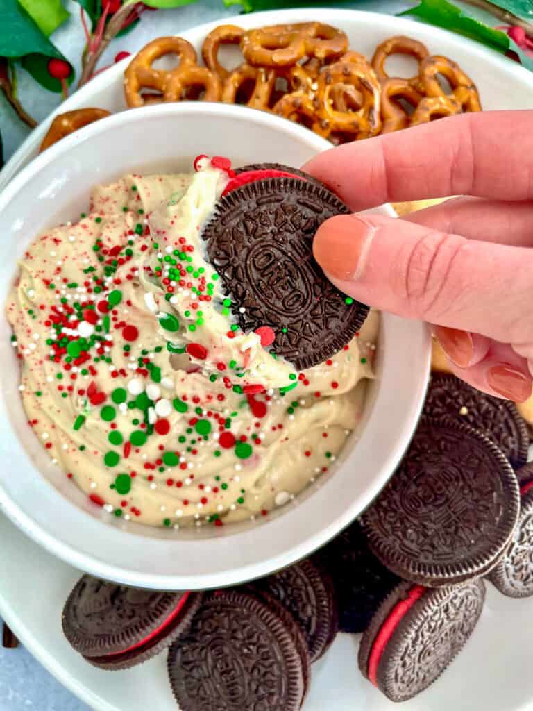 A hand dipping an oreo in sugar cookie dip in a small bowl.