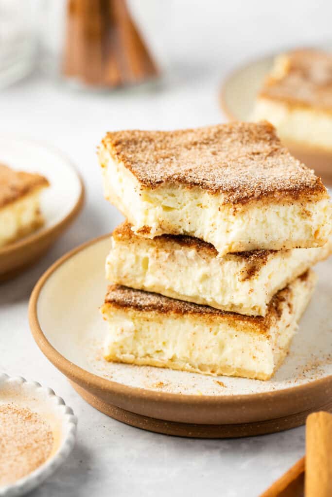 Churro protein cheesecake bars stacked on top of each other on a plate.