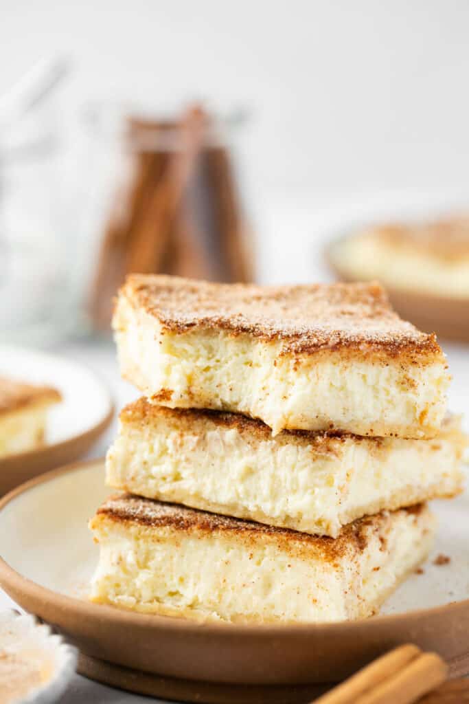 Three churro protein cheesecake bars stacked on top of each other on a small plate.