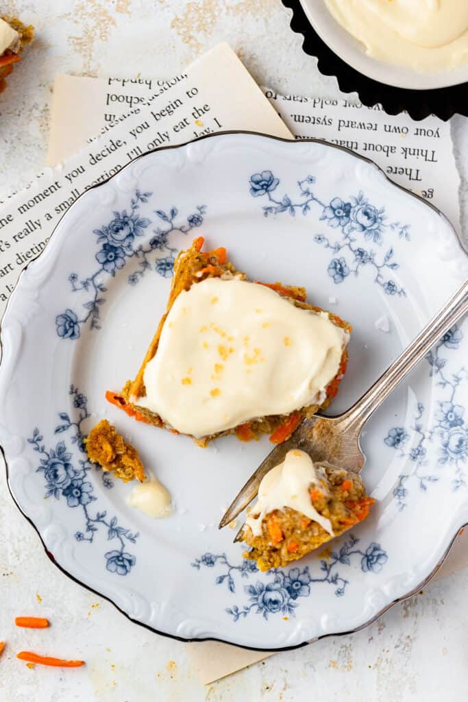 A serving of carrot cake oatmeal bake topped with vanilla maple cream cheese icing on a small plate with a fork.
