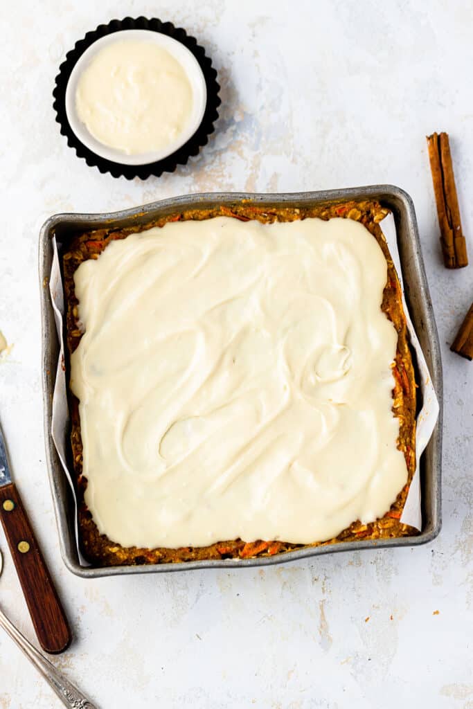 Carrot cake oatmeal bake topped with vanilla maple cream cheese icing in a baking pan.