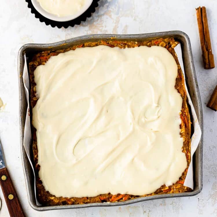 Carrot cake oatmeal bake topped with vanilla maple cream cheese icing in a baking pan.