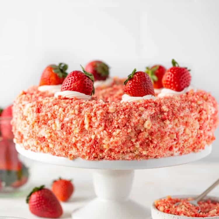 Strawberry crunch cake topped with straberries on a cake stand.