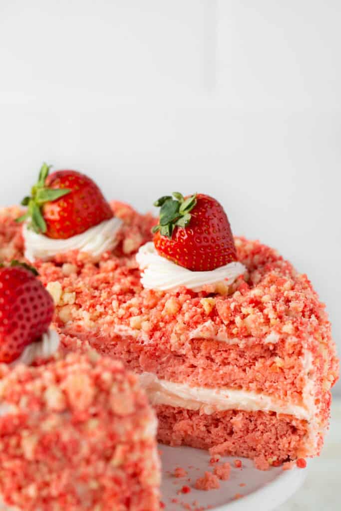 Zoomed in view of strawberry crunch cake topped with strawberries with a slice missing.