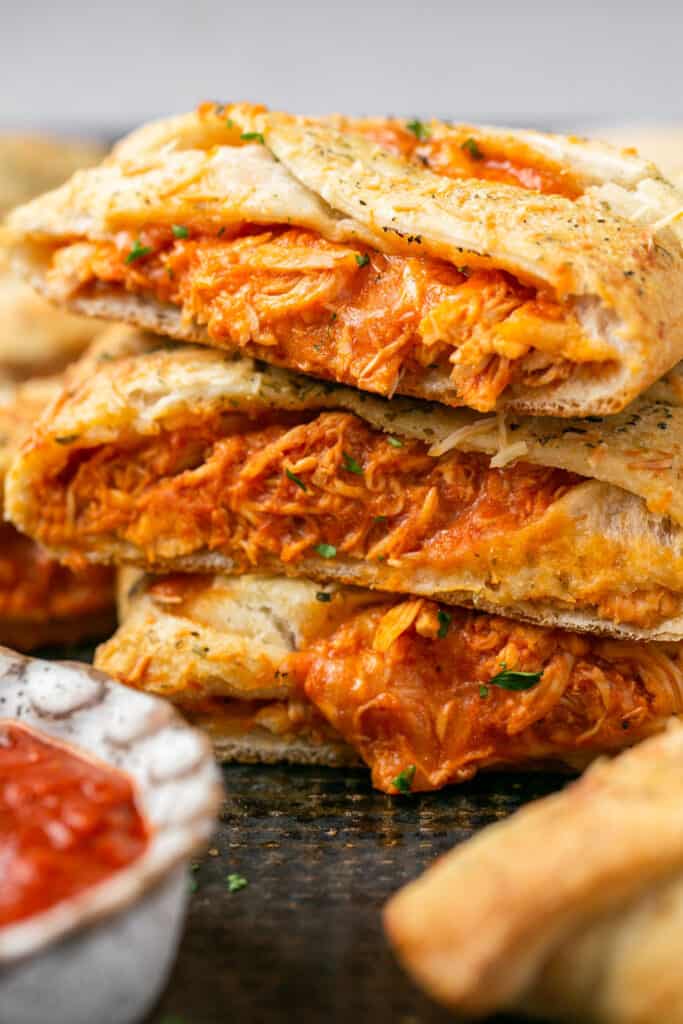 Zoomed in view of chicken parmesan stromboli cut into pieces on a tray with marinara sauce.