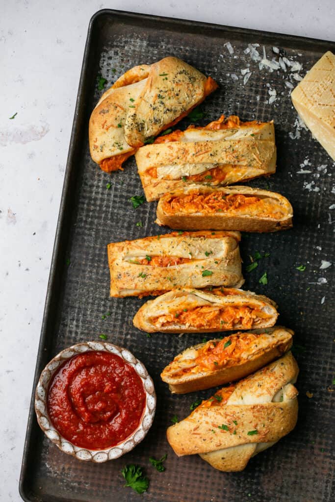 Chicken parmesan stromboli cut into pieces on a tray with marinara sauce.