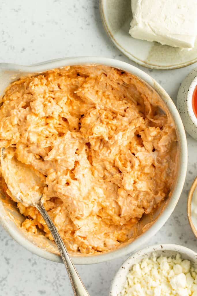 Buffalo chicken dip being mixed together in a bowl with a spoon.