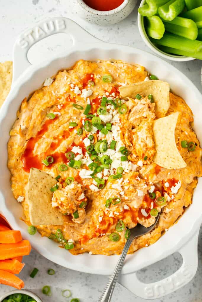 Healthy buffalo chicken dip recipe in a serving bowl topped with green onion and feta with tortilla chips being dipped in.