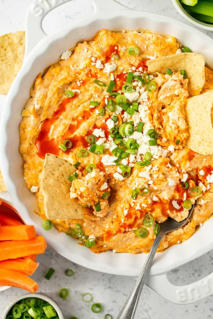 Healthy buffalo chicken dip recipe in a serving bowl topped with green onion and feta with tortilla chips being dipped in.